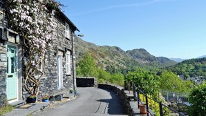 A stone building with a green door labeled "Carrie's Cafe," a paved road, and a mountainous landscape in the background. - 2 bedroom accommodation in Coniston (Coniston)
