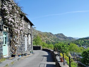 A stone building with a green door labeled "Carrie's Cafe," a paved road, and a mountainous landscape in the background.