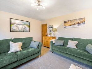 A cozy living room with two green sofas, a wooden cabinet, and artwork on the walls. - 2 bedroom accommodation in Coniston (Coniston)