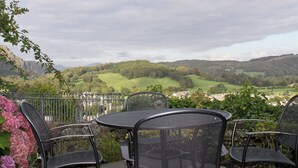 A patio with metal chairs and a table, overlooking a green landscape with hills. - 2 bedroom accommodation in Coniston (Coniston)