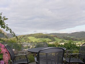 A patio with metal chairs and a table, overlooking a green landscape with hills.