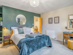 Une chambre à coucher comprenant un lit, des tables de chevet, une commode, un miroir et une porte donnant sur une autre pièce.