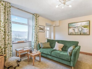 A cozy living room with a green sofa, a wooden coffee table, and a small table with a kettle and cups.