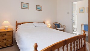 Un dormitorio con cama de madera, lámparas de noche, cómoda de madera y una silla de mimbre.