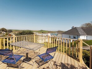 A wooden deck with a glass table and two chairs, overlooking a coastal area with houses and hills. - Berrystead Upper Flat (Allenhayes)