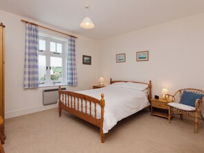 A bedroom with a wooden bed, a window with curtains, a bedside table with a lamp, a chair, and two wall-mounted pictures. - Berrystead Upper Flat (Allenhayes)