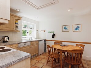 A kitchen with wooden cabinets, a dishwasher, a stove, a sink, and a dining table with chairs. - Berrystead Upper Flat (Allenhayes)