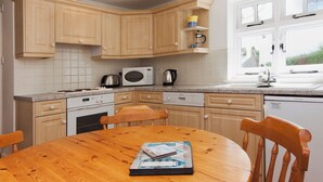 Una cocina con armarios de madera, microondas, hervidor de agua y una mesa de comedor con sillas.