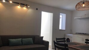 Una sala de estar con sofá, una mesa de comedor con sillas, una zona de cocina con estufa y una ventana.