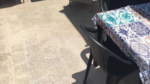 Una terraza con mobiliario de mimbre, incluyendo sillas y una mesa, y un mantel estampado en la mesa.