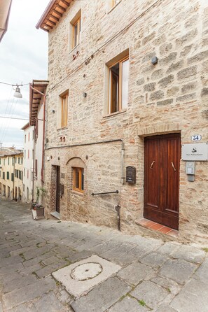 Un bâtiment en pierre avec une porte et des fenêtres en bois, une enseigne portant le numéro 34, et un petit espace extérieur agrémenté d’une plante en pot.