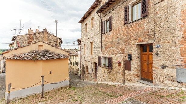 A narrow cobblestone street with historic buildings, a chain-link fence, and a wooden door with a number plaque. - Colle di Val d'Elsa - Siena - Apt Pink - B (Colle di Val d'Elsa)