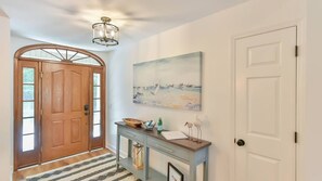 Un couloir avec une porte en bois, un tableau représentant une scène de plage, une console sur laquelle est posée une lampe, et une porte blanche.