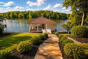 A lakeside cabin with a dock, a stone pathway, and a grassy lawn.