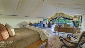 A tented accommodation with a bed, a desk, and a chair.
