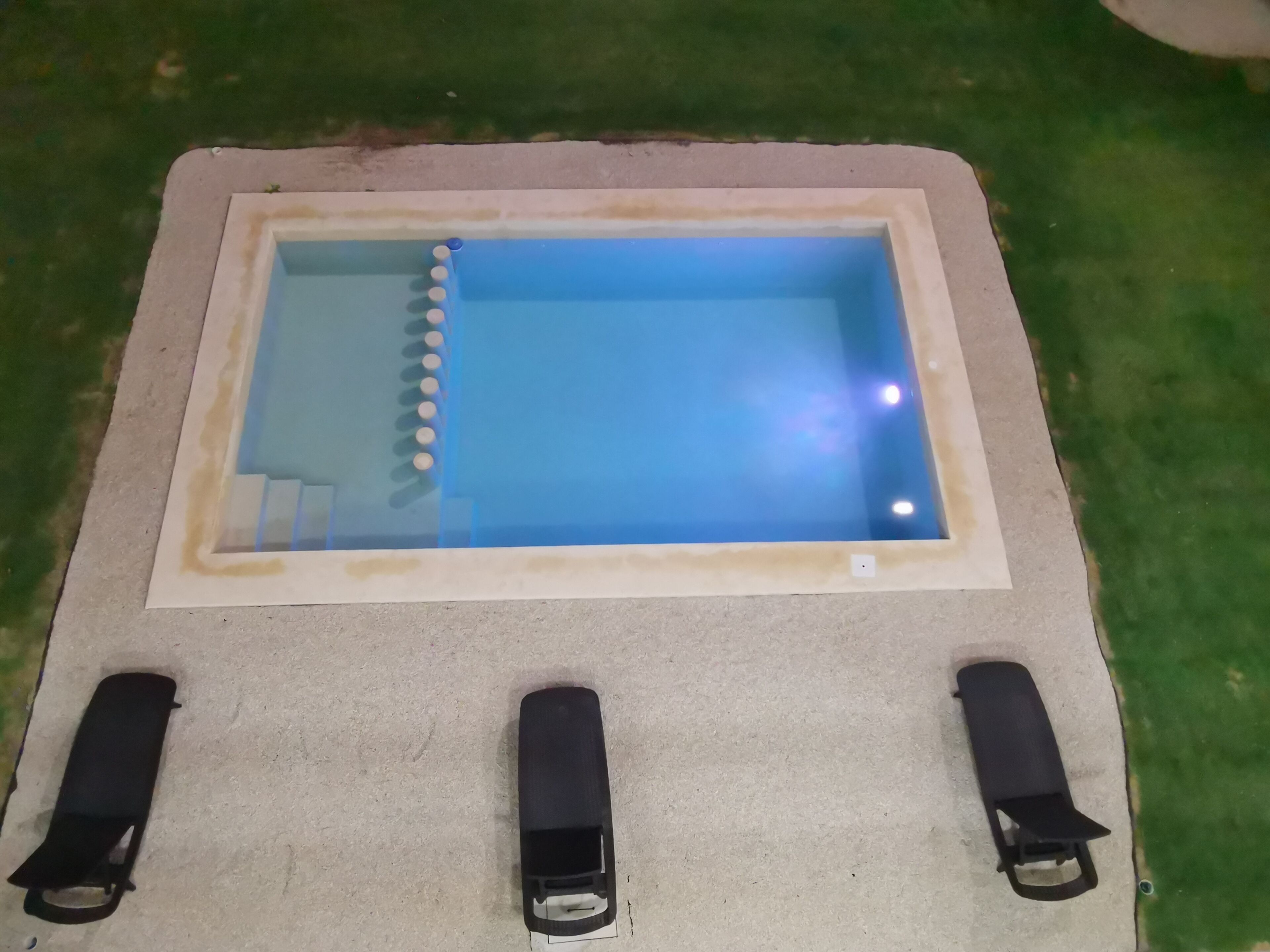 A pool with a clear blue water surface, surrounded by a concrete deck.