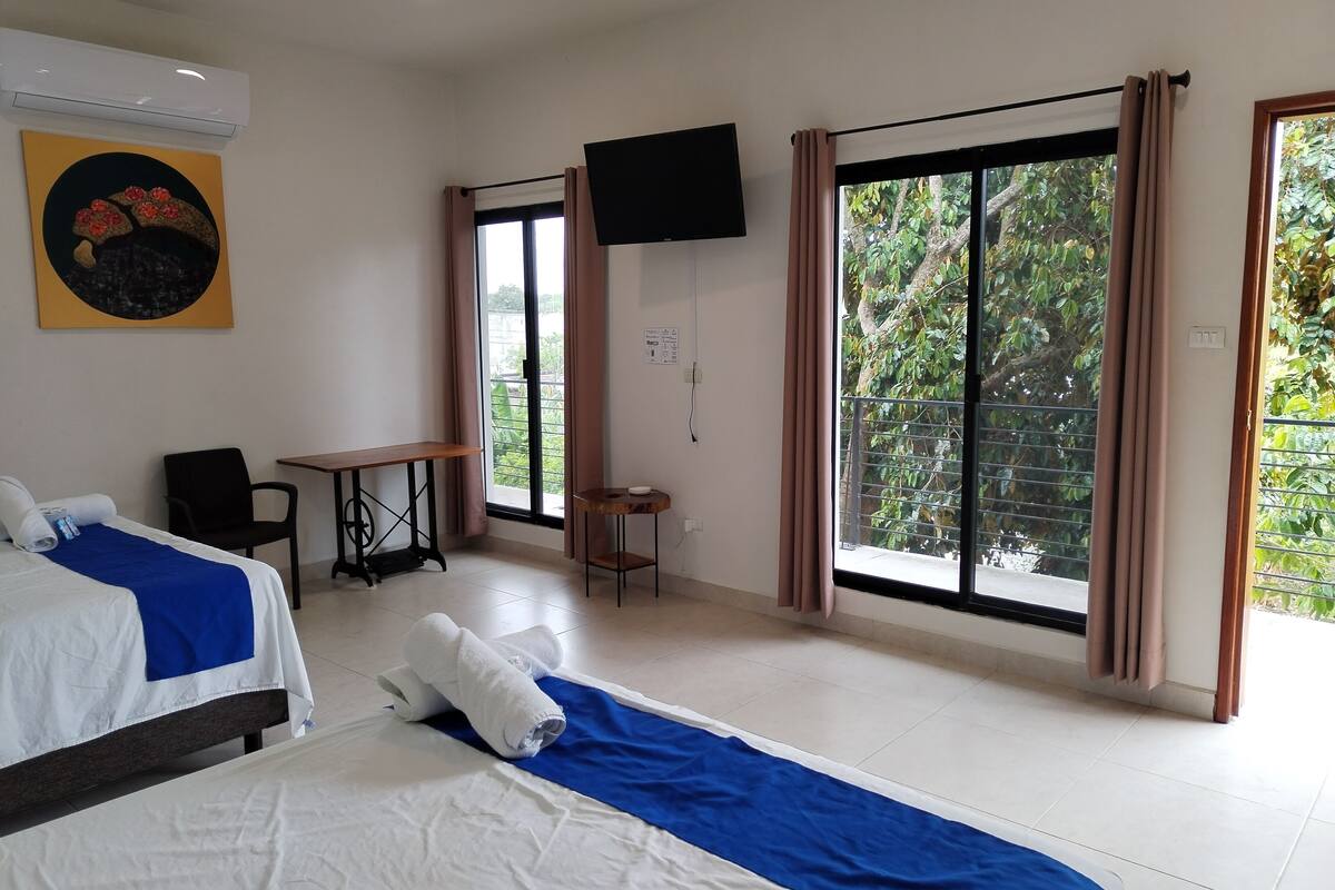 A hotel room with a bed, a desk, a chair, a TV, and large windows with curtains.