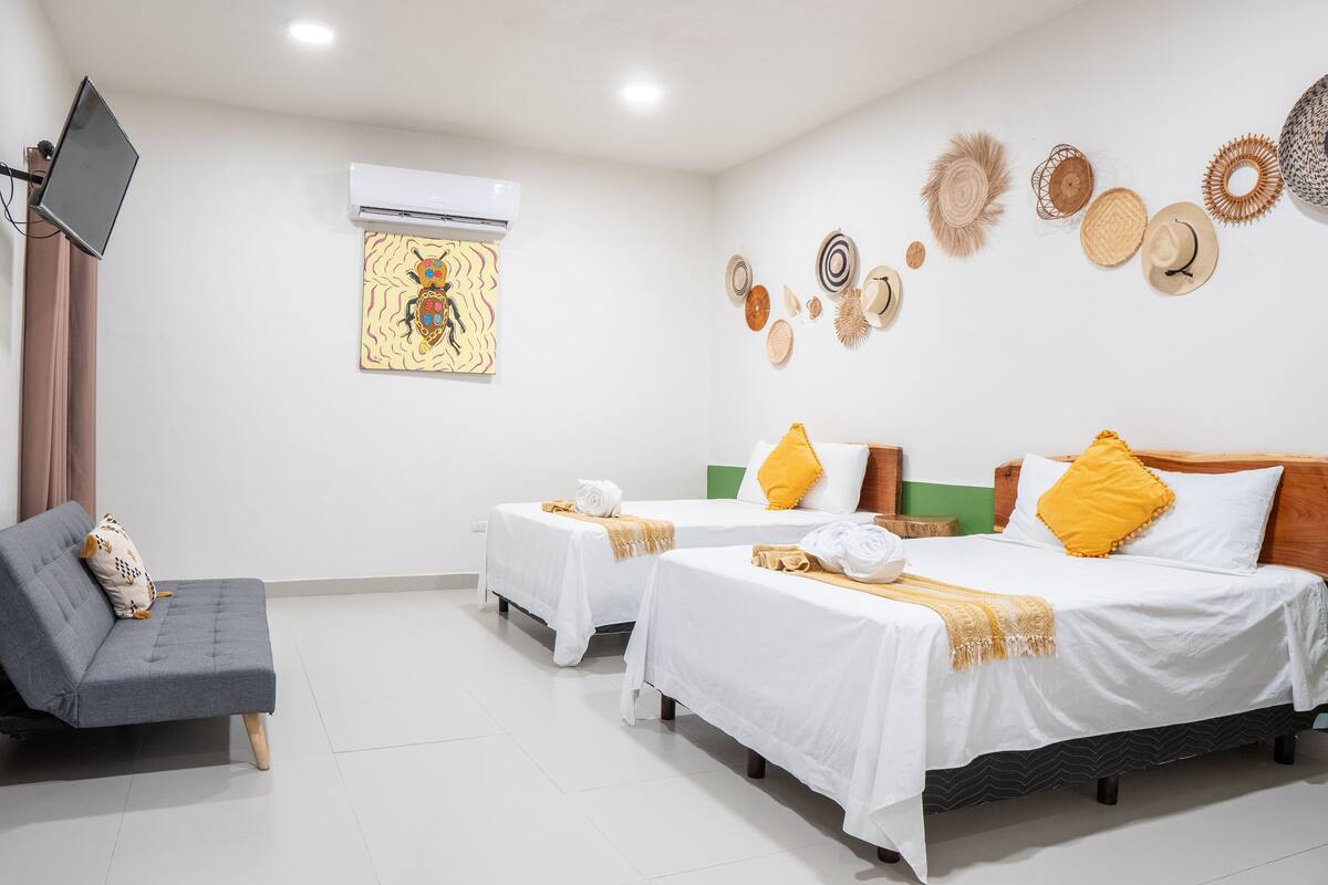 A hotel room with two single beds, a sofa, and a flat-screen TV.