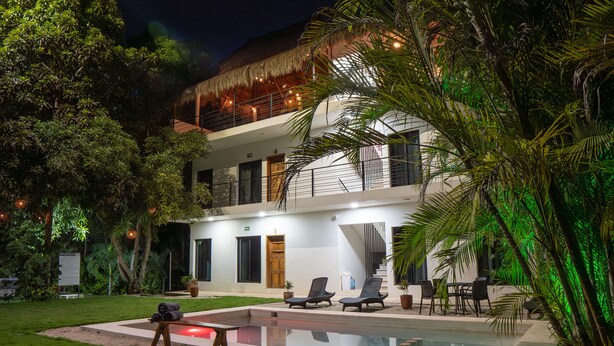 A two-story building with a pool, lounge chairs, and a staircase.