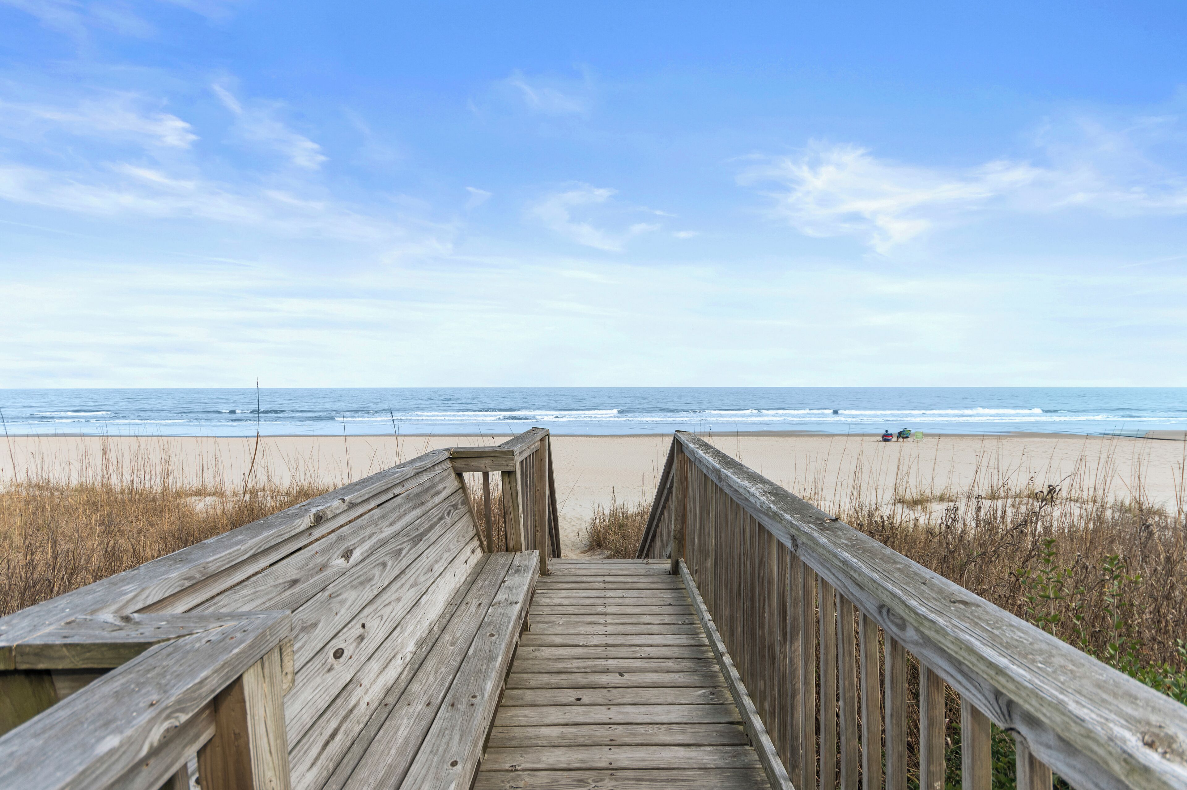 A wooden boardwalk leading to a beach with a clear sky.
