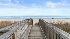Un paseo marítimo de madera que conduce a una playa con cielo despejado.