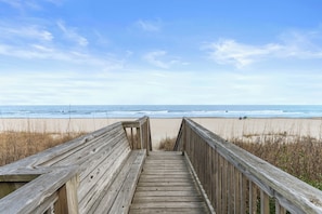 A wooden boardwalk leading to a beach with a clear sky.