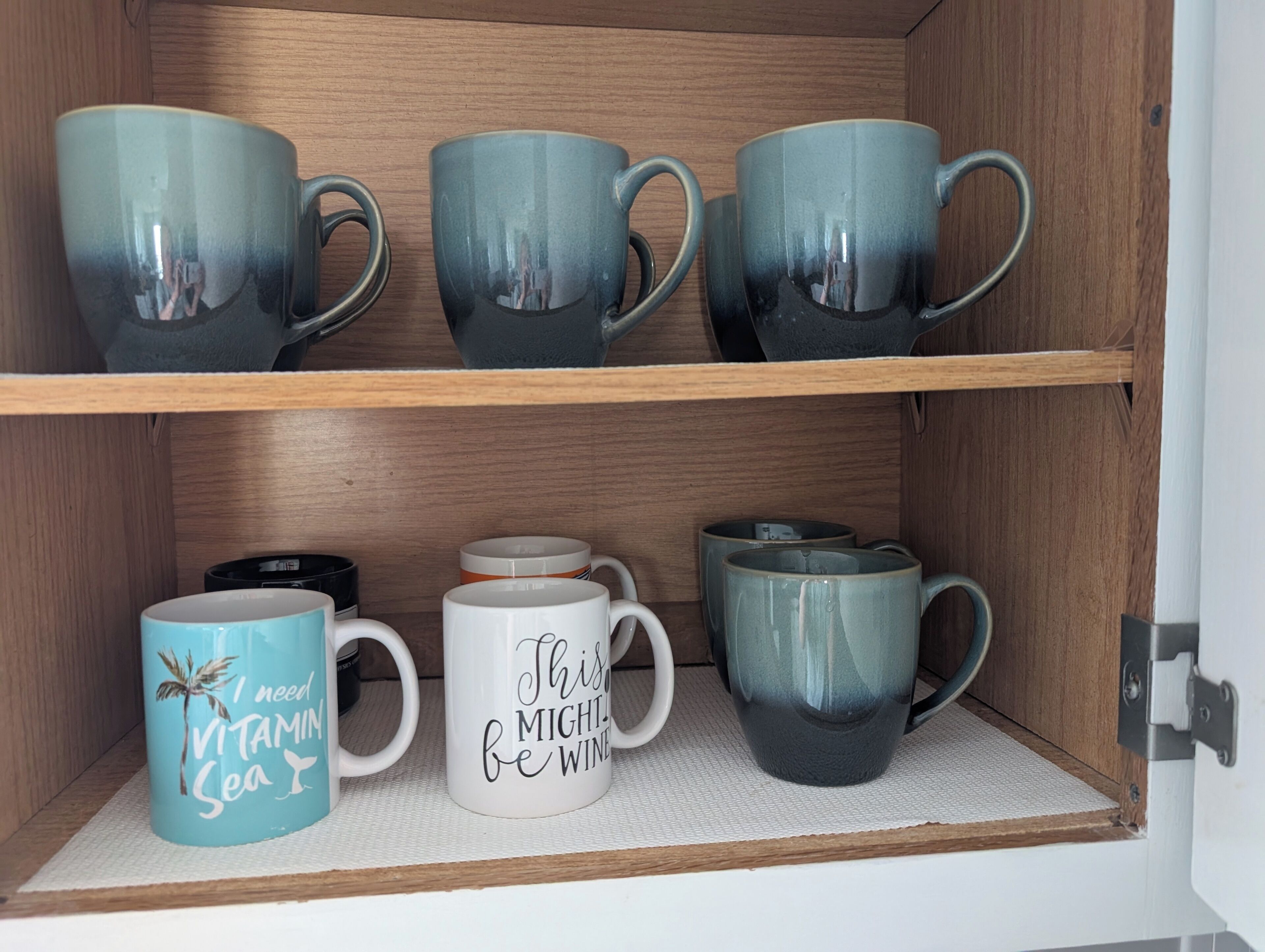 A wooden cabinet with two shelves holding various ceramic mugs.