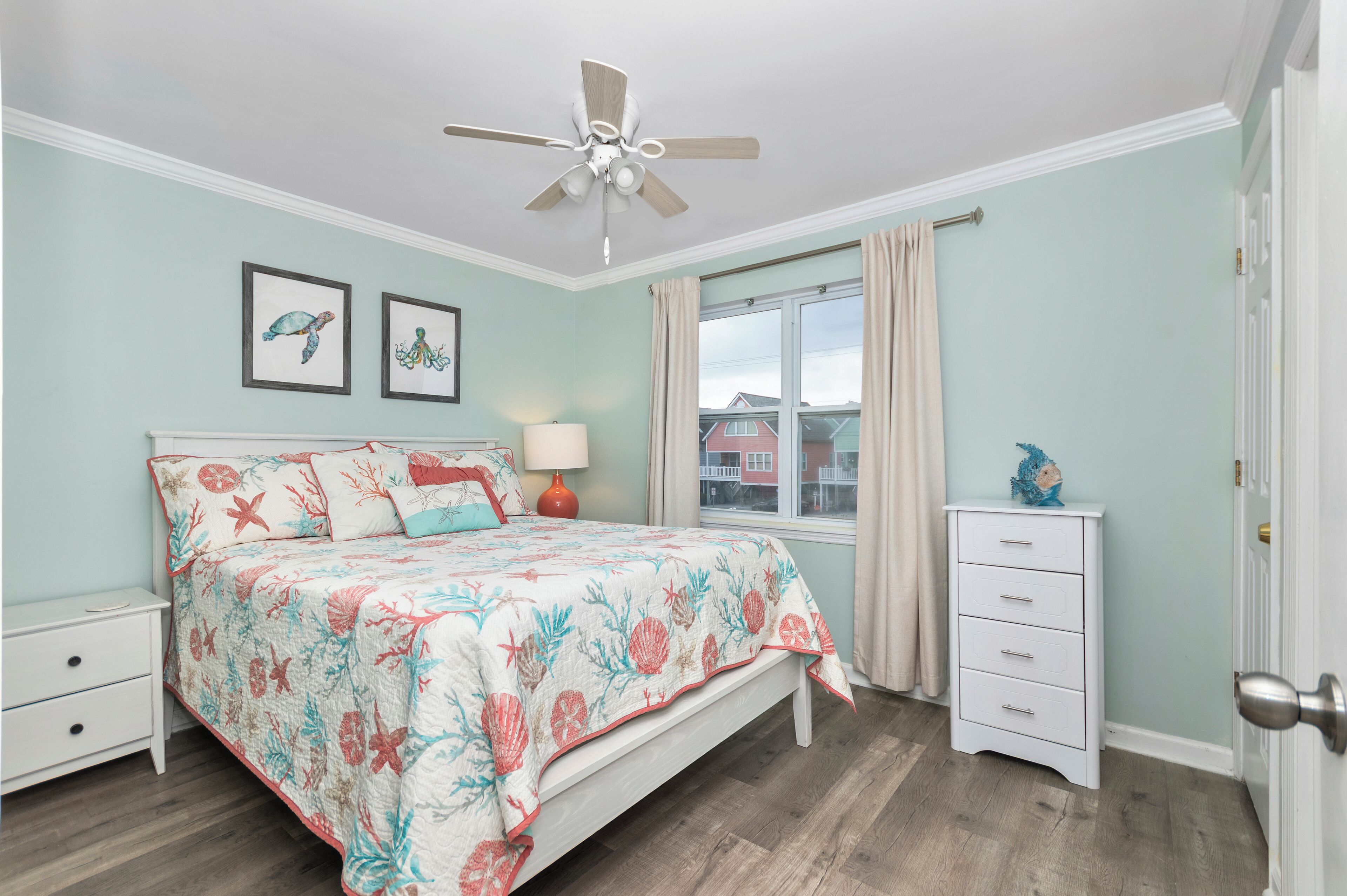 A bedroom with a bed, nightstand, dresser, ceiling fan, and a window with curtains.