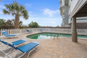 A pool area with lounge chairs, a palm tree, and a white fence.
