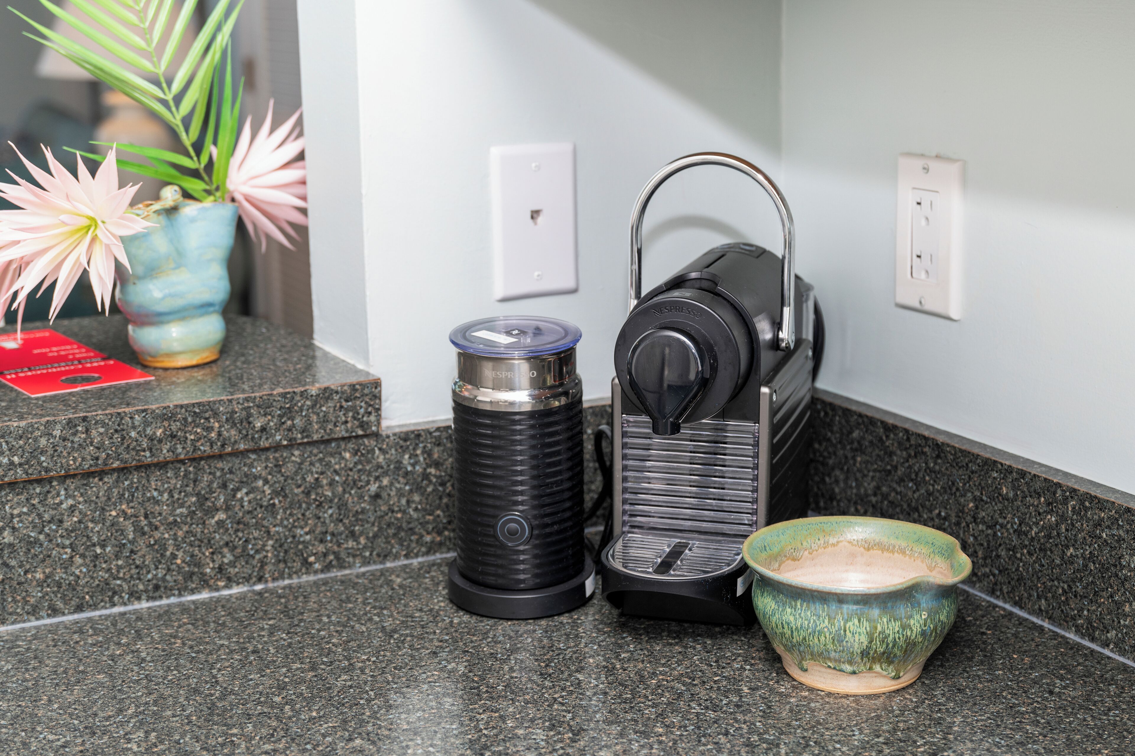 Una encimera de cocina con una cafetera, un termo y un tazón de cerámica.