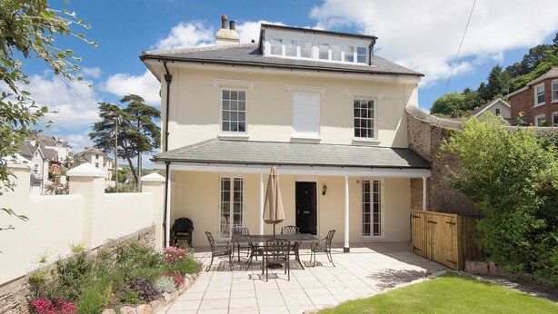 A two-story house with a patio area featuring a table and chairs, surrounded by a garden with various plants and flowers. - 5 bedroom accommodation in Victoria Road (Victoria Road)