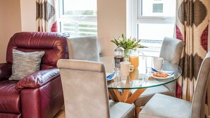 Ein modernes Wohnzimmer mit einem Glastisch, Ledersesseln und Blick ins Freie durch große Fenster.