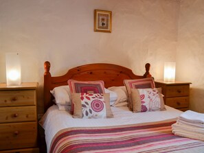 Un lit bien fait, recouvert d’une couverture à rayures, deux tables de chevet avec des lampes et un tableau encadré au mur.
