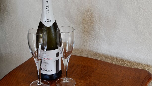 A bottle of Brut Italy wine with two glasses on a wooden table.