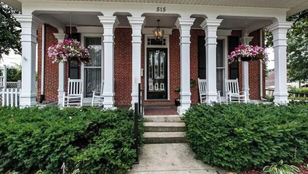 A brick building with a white porch, number 515, and two white chairs with hanging flower baskets. - Federalist style home close to down town minutes from the Field of Dreams! (Dyersville)