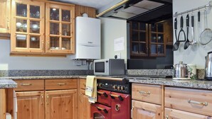Une cuisine avec des meubles de rangement en bois, un fourneau rouge, un four à micro-ondes et divers ustensiles de cuisine.
