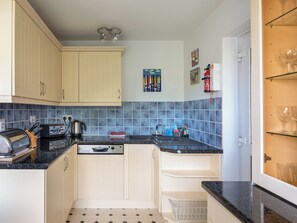 A compact kitchen with light-colored cabinets, a black countertop, and blue-tiled backsplash. - 3 bedroom accommodation in Salcombe (Salcombe)