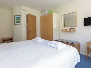 A hotel room with a large bed, a wooden wardrobe, a small bedside table, a wicker chair, and a flat-screen TV mounted on the wall.