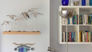 Et værelse med en hvid pejs, en bogreol fyldt med bøger, dekorativ vægkunst og en gulvlampe.