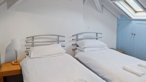 A twin room with two beds, a skylight, a wooden nightstand, and a blue wardrobe. - 2 bedroom accommodation in Fore St (Fore St)