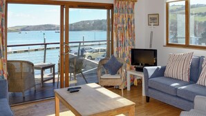 A spacious living room with a large window overlooking a body of water, furnished with a sofa, chairs, and a television. - 2 bedroom accommodation in Fore St (Fore St)