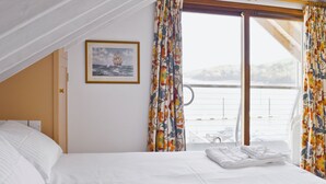 A hotel room with a large bed, a window with curtains, a painting on the wall, and a view of the sea. - 2 bedroom accommodation in Fore St (Fore St)