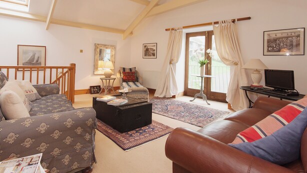 A spacious living room with a high ceiling, a sofa, a coffee table, a television, and a window with curtains. - 3 bedroom accommodation in Shadycombe Road (Shadycombe Road)