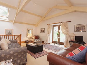 A spacious living room with a high ceiling, a sofa, a coffee table, a television, and a window with curtains. - 3 bedroom accommodation in Shadycombe Road (Shadycombe Road)
