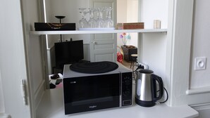 A kitchen with a microwave, kettle, and glassware on shelves. - Apartment du Puits Salé (Lons-le-Saunier)