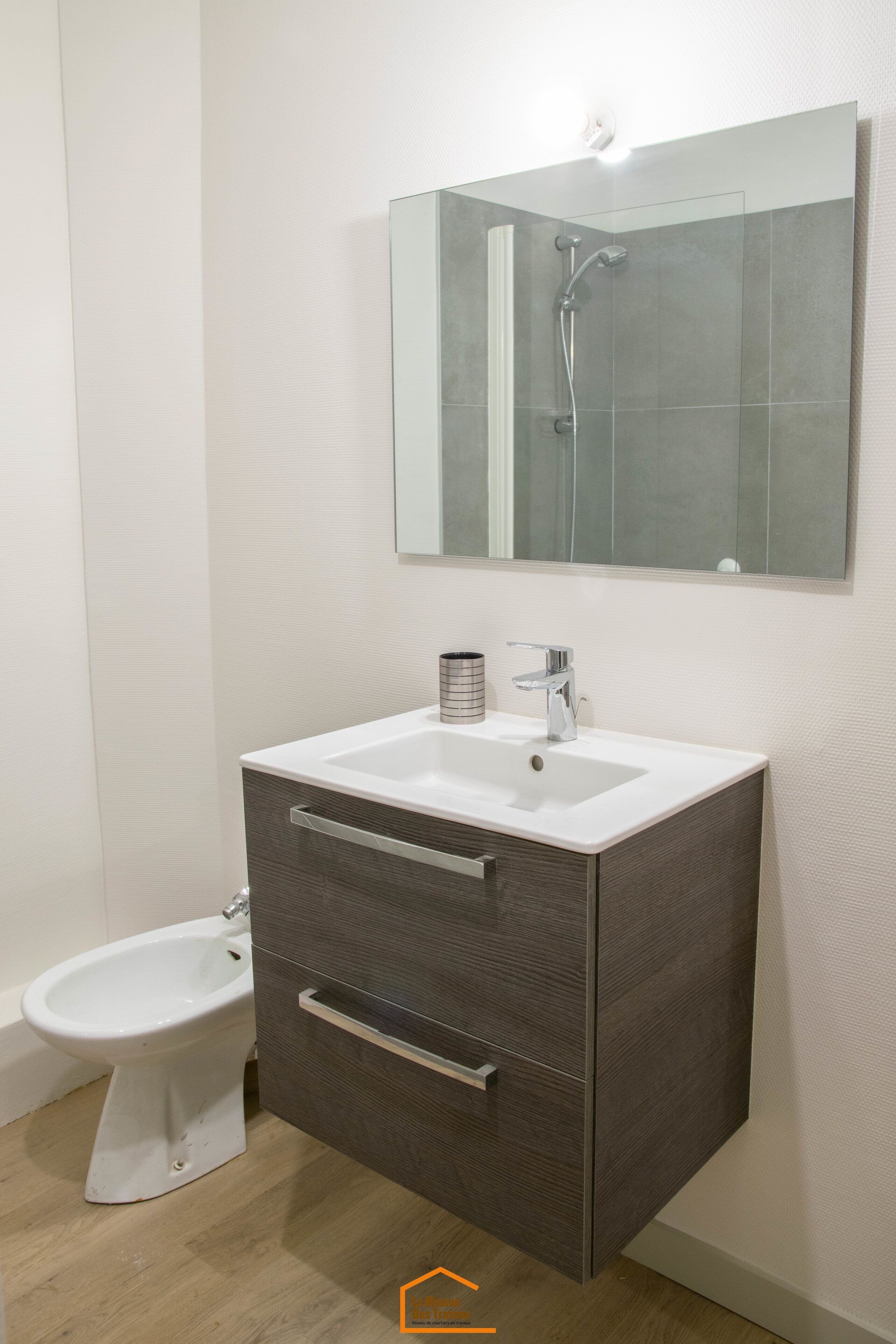 A bathroom with a white sink, dark wood vanity, a mirror, and a bidet.