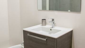 A bathroom with a white sink, dark wood vanity, a mirror, and a bidet.