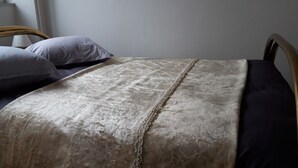 A bed with a beige blanket and two pillows, a wooden headboard, and a radiator in the background. - Apartment du Puits Salé (Lons-le-Saunier)