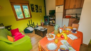 A cozy living room with a green sofa, a dining table set with breakfast, and a kitchen area with wooden cabinets and a stove. - Rural House With Jacuzzi and Fireplace in the Room for 2 People (Riello)
