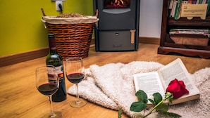 A cozy reading area with a wicker basket, a wine bottle, two wine glasses, a fluffy rug, a book, and a rose. - Rural House With Jacuzzi and Fireplace in the Room for 2 People (Riello)